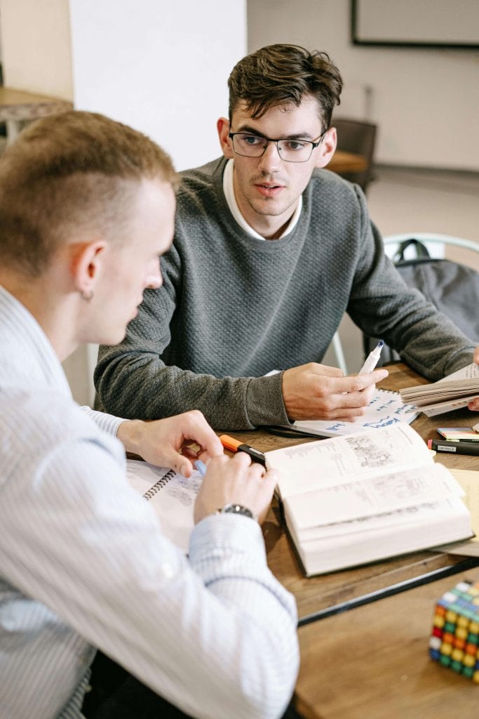 Two young male students discussing notes and assignments in a classroom, highlighting collaborative learning and teamwork.