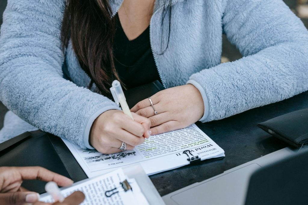 A student in a cozy blue fleece jacket highlighting text on a worksheet, emphasizing active studying and note-taking strategies.