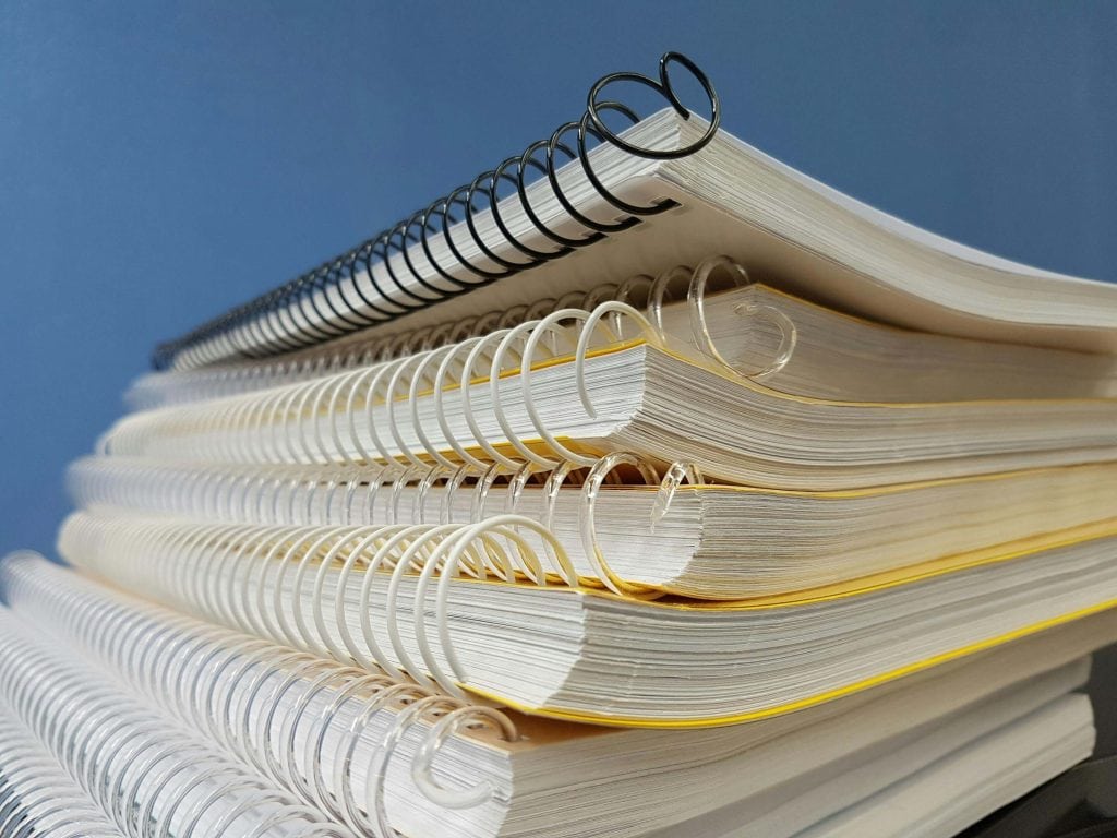 A neatly stacked pile of spiral-bound notebooks against a blue background, representing academic preparation and organization.