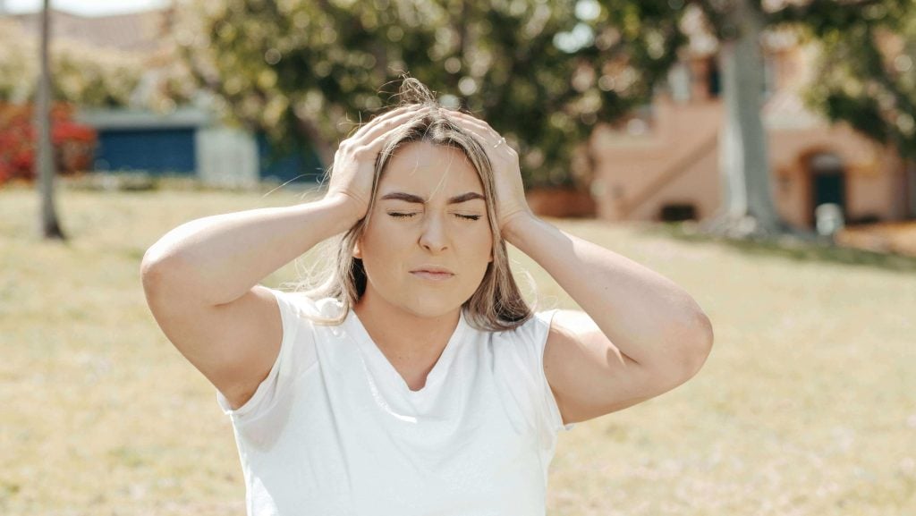 A woman outdoors holds her head in frustration, illustrating the emotional challenges parents face when supporting children with big emotions and self-regulation struggles.