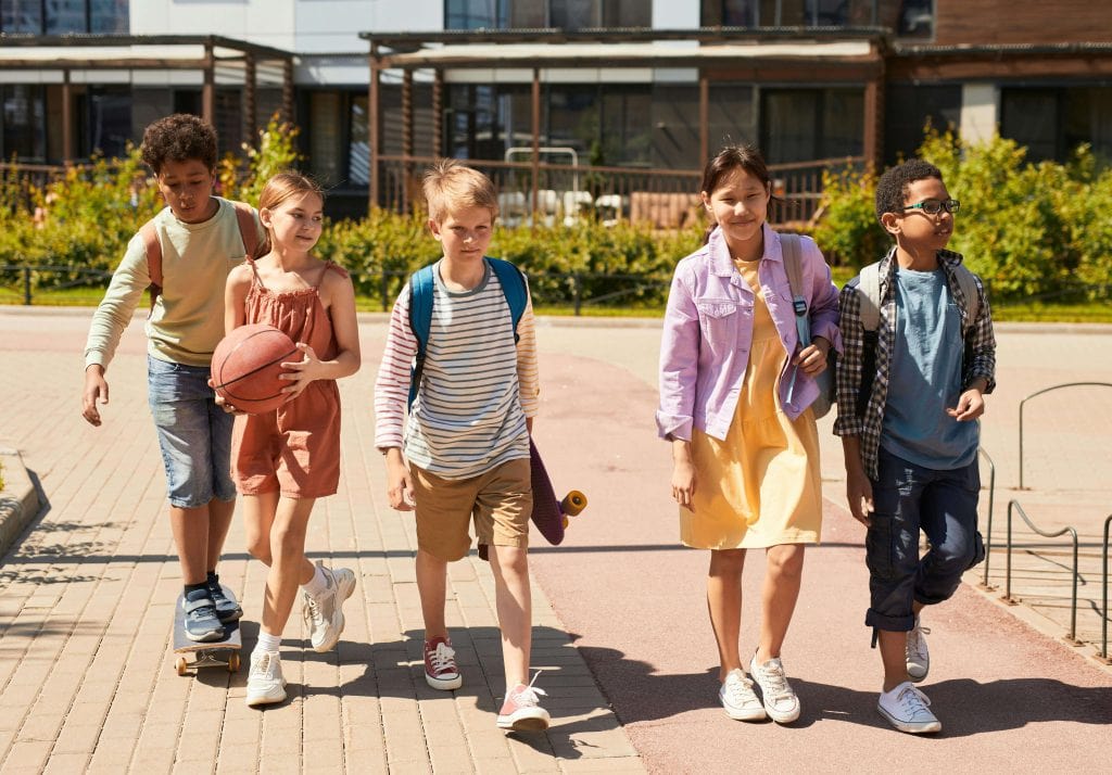 A diverse group of children walk together outside a school, representing the importance of peer relationships, academic support, and executive functioning skills for students with ADHD.