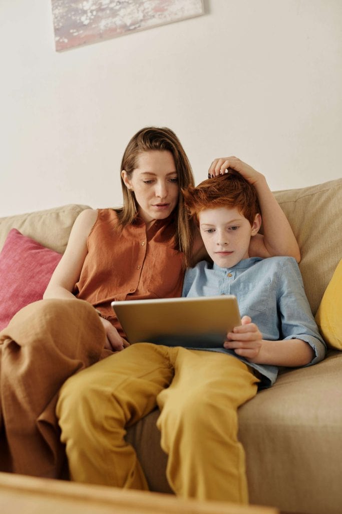 A mother and her child sitting on a couch, looking at a tablet together, illustrating how parents can support AAC use for communication at home for autistic kids.
