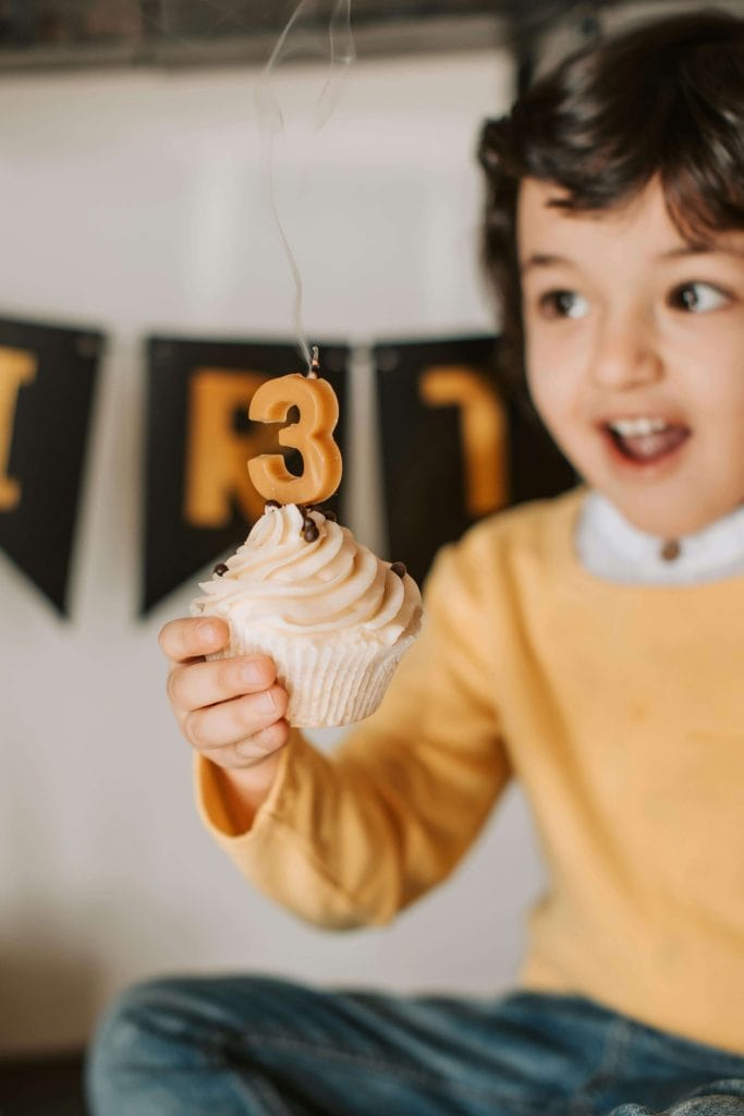 A three-year-old child excitedly holds a cupcake with a number 3 candle, representing a common age when parents notice speech delays. 3 year old speech delay not autism