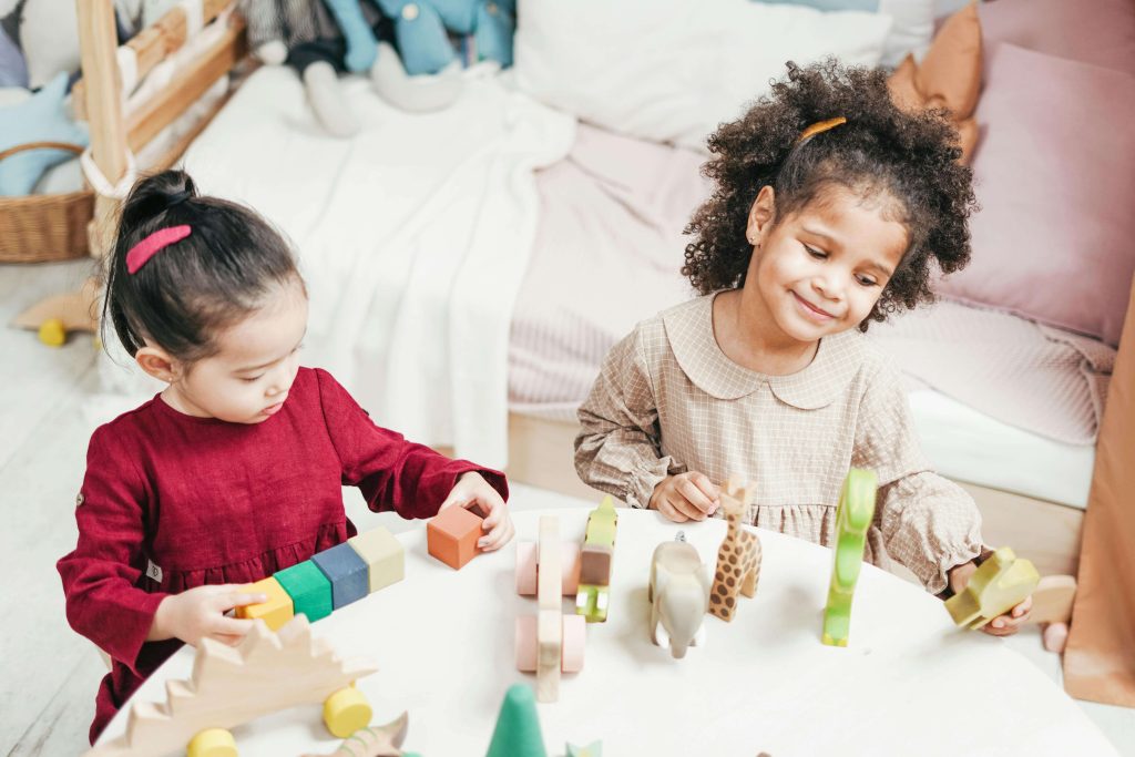 Two young children play with toy animals and wooden blocks, encouraging pretend play and language use during early development.
