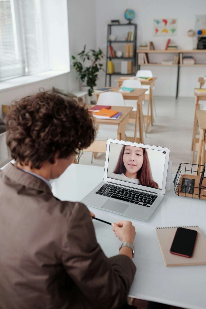 A teacher or therapist speaks with a parent during a virtual meeting in a classroom setting, discussing speech and language development in young children.