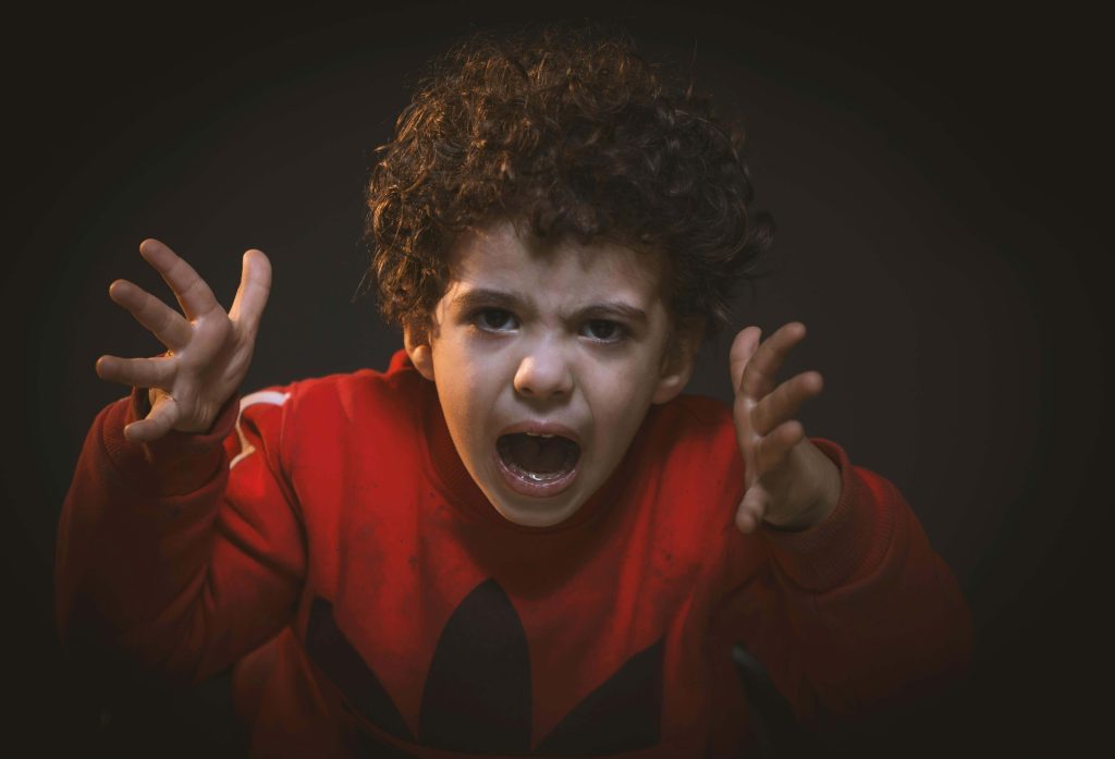 An upset child yells and gestures with frustration, potentially experiencing behavioral signs of sensory overload or shutdown in autism