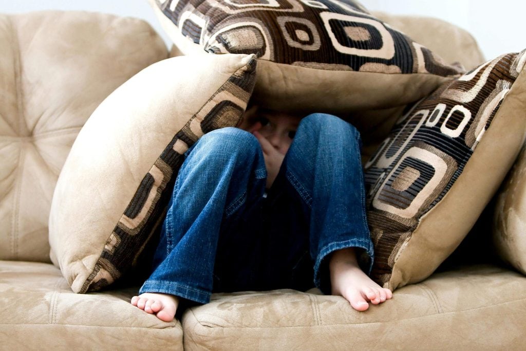 A young child hides under couch cushions, possibly experiencing sensory overwhelm during an autism shutdown. autism shutdown symptoms
