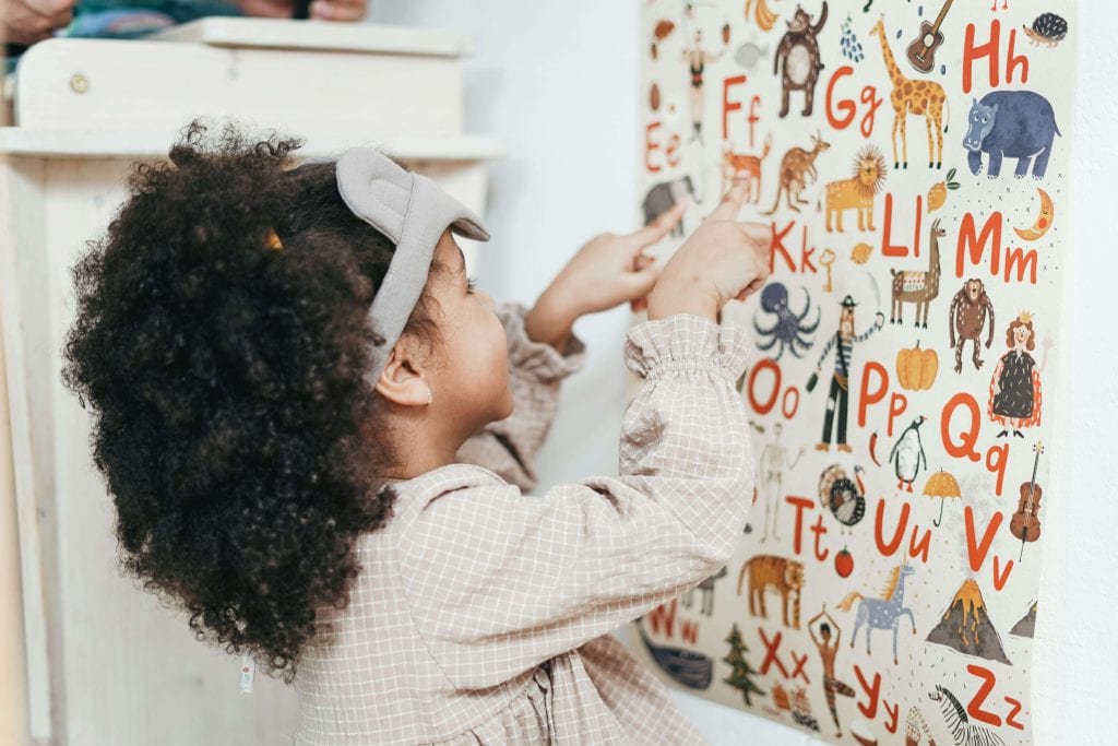 A young child points to letters on an alphabet chart, engaged in an early language activity to support speech and vocabulary development.