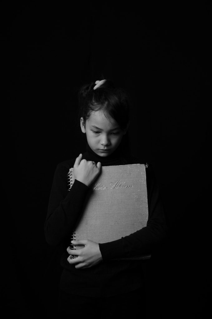 A quiet child holds a photo album against a dark background, suggesting isolation or inward withdrawal during an autistic shutdown