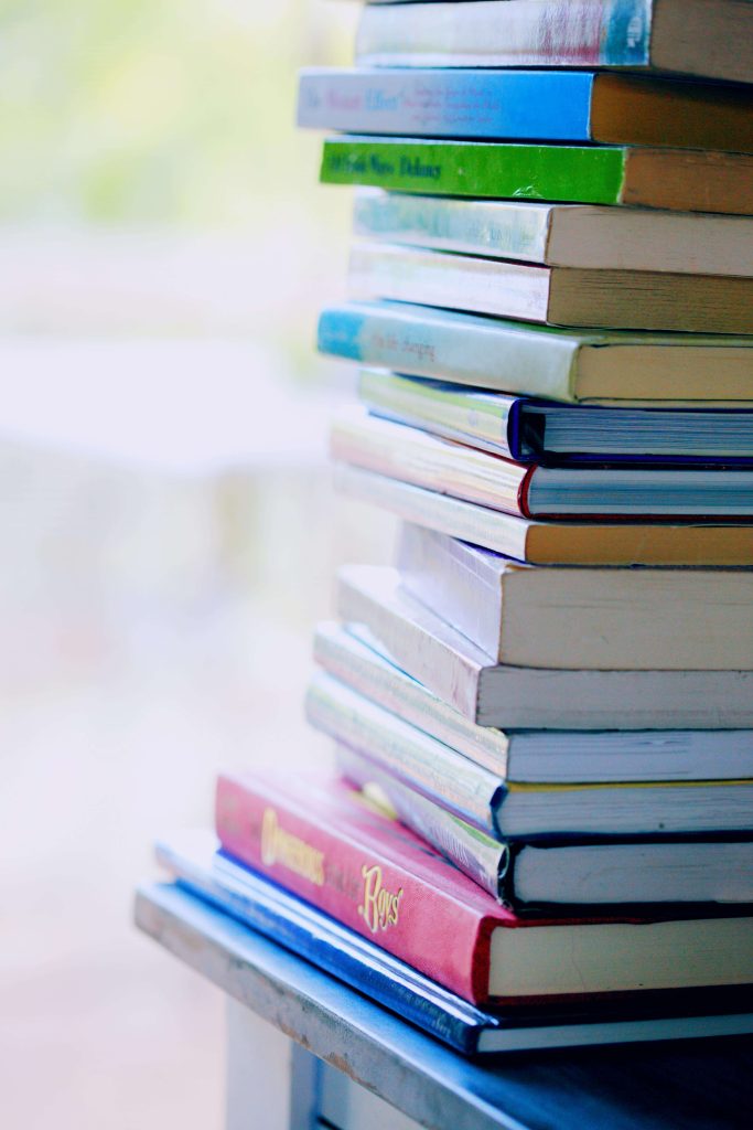 A tall stack of colorful children's books on a table, representing learning and literacy resources for parents navigating autism-related terms and acronyms.