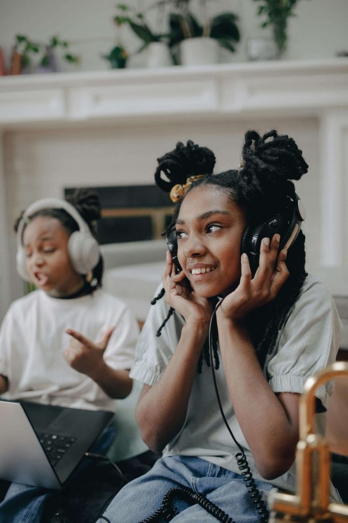 Two children wearing headphones and smiling while using a laptop, showing how headphones can be a helpful auditory sensitivity strategy for managing noise.