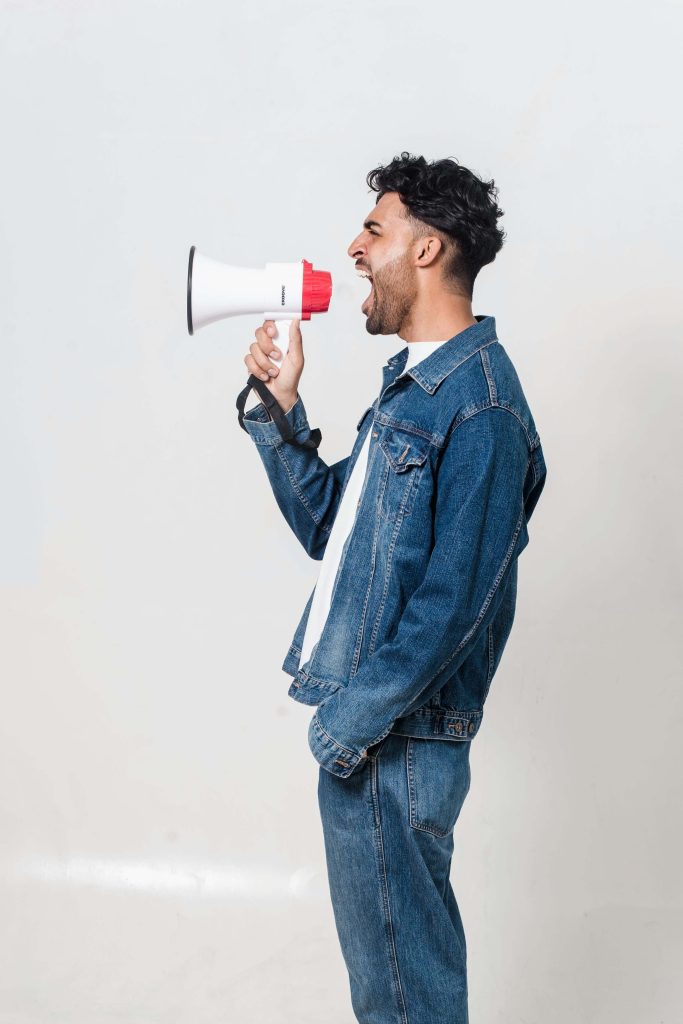 A man in a denim jacket yelling into a megaphone, representing challenges for individuals with auditory sensitivity and the need for effective auditory sensitivity strategies.