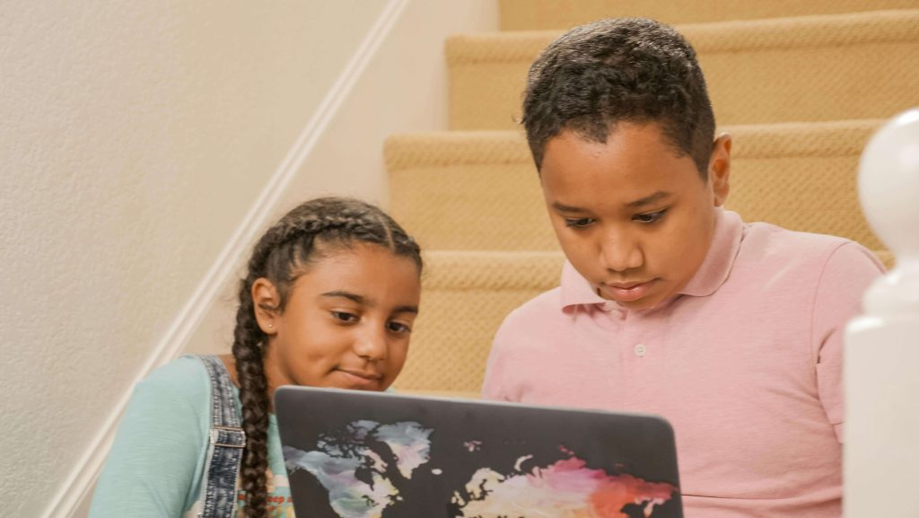 A boy and girl intently watching something on a laptop, suggesting a quiet, shared activity that supports auditory sensitivity strategies in a home environment.