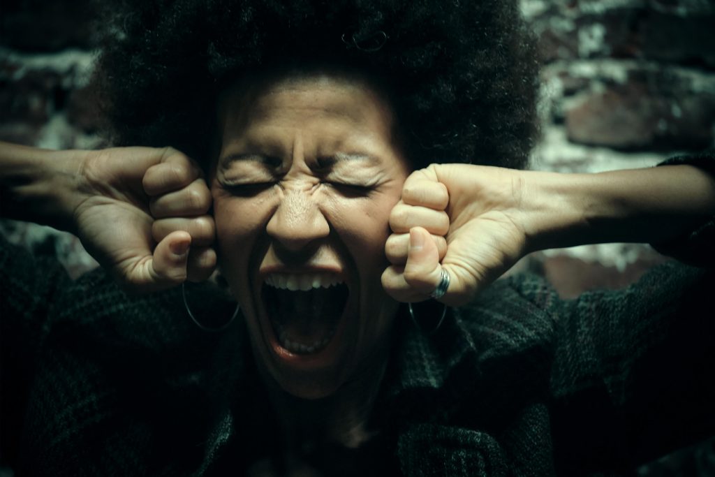 A distressed woman covering her ears and screaming, illustrating a strong reaction to overwhelming noise—an example of why auditory sensitivity strategies are important.